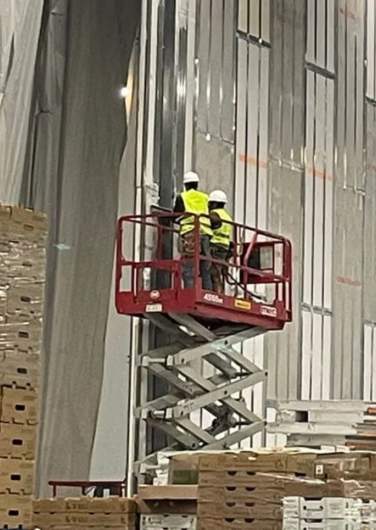 Workers on lift installing panel walls inside warehouse structure